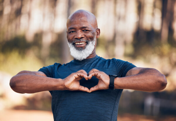 African American man smiling at camera with hands in shape of heart in front of chest