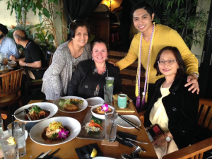 A man and three women gathered in front of a table with Asian dishes. 