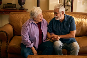 husband and wife hold hands on couch with white hair