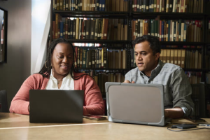 Woman and man sit at computers together smiling