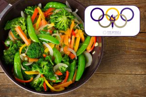 Colorful stir-fried vegetables including broccoli, snap peas, bell peppers, onions, and carrots in a pan on a wooden surface.