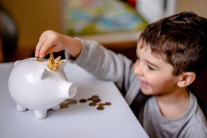 Smiling toddler inserting a coin into a piggy bank.