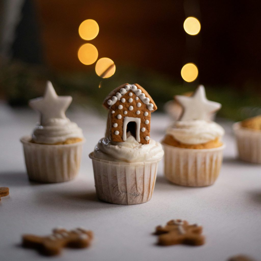 Three holiday themed cupcakes in front of christmas lights.