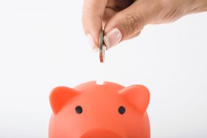 Hand dropping a coin into a piggy bank slot.