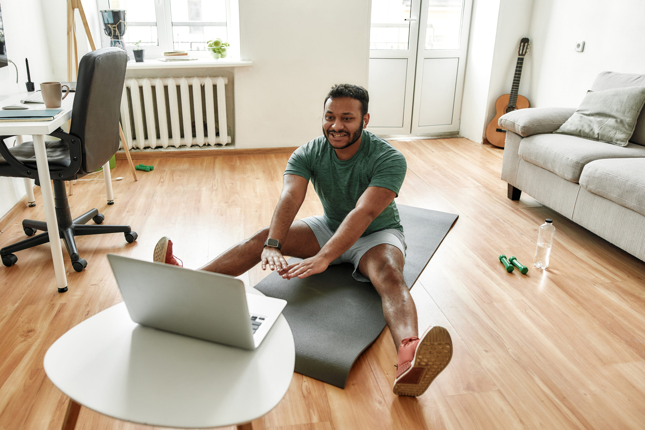 young man doing yoga on mat in living room in front of computer